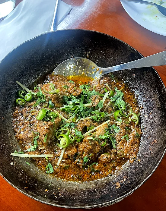Karahi in a black iron wok with green chilies and ginger